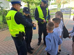 Policjanci przy szkole rozdają dzieciom odblaski.