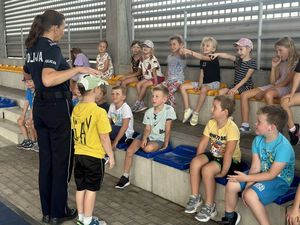 Pani policjant rozmawia z dziećmi siedzącymi przed nią na trybunach, obok niej stoi chłopiec.