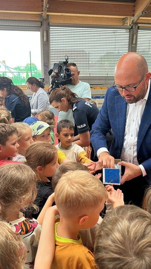 Dwie policjantki oraz Zastępca Prezydenta rozdają dzieciom odblaski