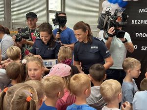 Policjantki rozdają odblaski grupie dzieci, która je otoczyła