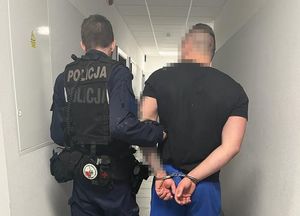 Umundurowany policjant prowadzi zatrzymanego mężczyznę.