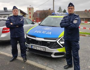 Policjanci stoją na tle radiowozu policyjnego.