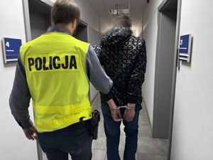 Policjant prowadzi zatrzymanego korytarzem komendy.