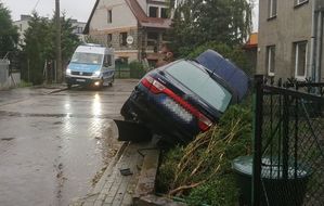 Samochód seat znajduje się po prawej stronie drogi, widać że najechał na płot, który też został zniszczony, natomiast pojazd jest przechylony na prawy bok. W tle po lewej stronie zdjęcia, po drugiej stronie ulicy stoi policyjny radiowóz.