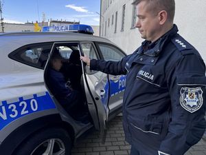 Policyjny radiowóz w którym z tyłu siedzi zatrzymany a drzwi do radiowozu zamyka policjant.