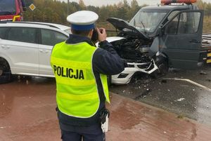 Policjant wykonuje dokumentację fotograficzną podczas wypadku, w tle widać zderzenie samochodów.