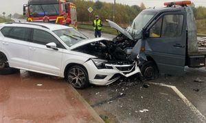 Zderzenie czołowo dwóch samochodów, w tle za nimi stoi policjant który wykonuje oględziny.