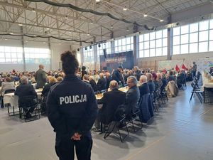 Policjantka stoi plecami do robiącego zdjęcie, a w tle siedzą przy stołach seniorzy