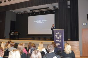 Policjantka stoi na scenie sali konferencyjnej i prowadzi spotkanie z młodzieżą.