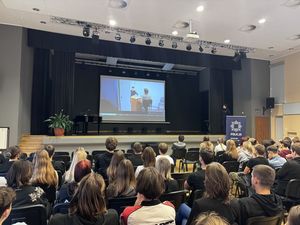 Policjantka stoi na scenie sali konferencyjnej i prowadzi spotkanie z młodzieżą.