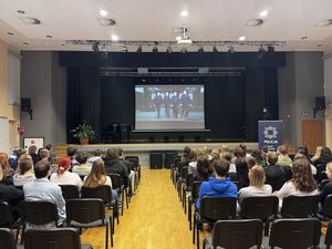 Policjantka stoi na scenie sali konferencyjnej i prowadzi spotkanie z młodzieżą.