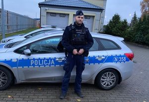 Policjant stoi przed radiowozem.