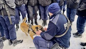 Policjant przykucnął obok swojego psa a młodzież otoczyła go w koło.