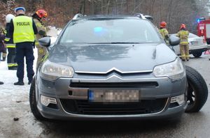 Na zaśnieżonej drodze stoi samochód citroen, obok po lewej stronie za pojazdem stoi policjant ze strażakami.