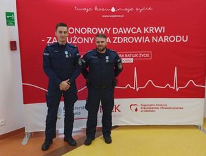 Dwaj policjanci stoją na czerwonym tle związanym z Honorowym Oddawaniem Krwi.