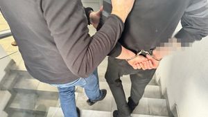 Policjant w ubiorze cywilnym sprowadza zatrzymanego w kajdankach po schodach w komendzie