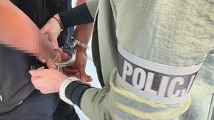 Policjantka zakłada kajdanki zatrzymanemu na ręce trzymane z tyłu.