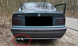 Samochód bmw stoi na drodze leśnej. Wydech tego samochodu został zaznaczony na zdjęciu czerwonym kołem.