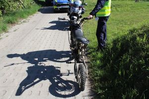 Policjant stoi przy motocyklu, w tle widać także radiowóz