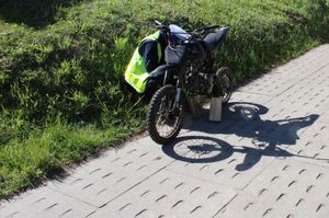 Policjant kuca za motocyklem sprawdzając uszkodzenia i stan techniczny pojazdu.