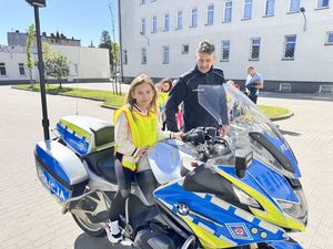 Dziewczynka siedzi na policyjnym motocyklu obok asekuruje ją policjant.