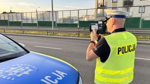 Policjant stoi przy drodze i wykonuje pomiar prędkości.