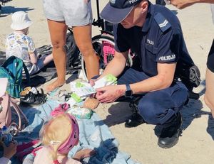 Policjanci  na plaży rozdają opaski niezgubki i ulotki o konkursie