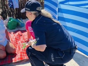 Policjanci  na plaży rozdają opaski niezgubki i ulotki o konkursie