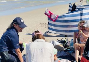 Policjanci  na plaży rozdają opaski niezgubki i ulotki o konkursie