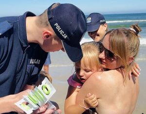 Policjanci  na plaży rozdają opaski niezgubki i ulotki o konkursie