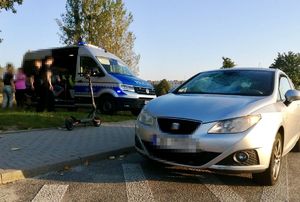 Na drodze stoi seat, obok hulajnoga a za nią radiowóz, przy którym rozmawiają jakieś osoby