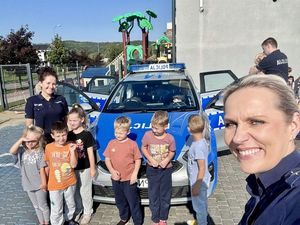 Zdjęcie typu selfie w tle dzieci z policjantką i radiowóz za nimi