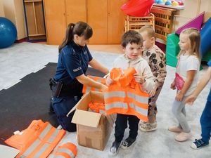 Policjantka wręcza dzieciom kamizelki odblaskowe.