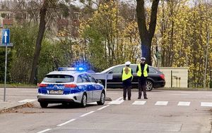 Policyjny patrol stoi w rejonie skrzyżowana , w tle stoi także policyjny radiowóz na sygnałach.