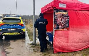 Policjant kontroluje punkt sprzedaży alkoholu , obok stoi policyjny radiowóz