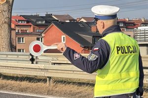 Policjant daje sygnał tarczą do zatrzymania się kierowcy samochodu