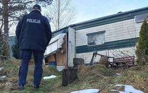 Policjant idzie w kierunku opuszczonej zniszczonej przyczepy samochodowej typu holenderskiego