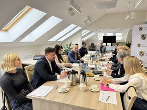 W trakcie spotkania komisji zdrowia psychicznego jej członkowie siedzą przy stole konferencyjnym i rozmawiają