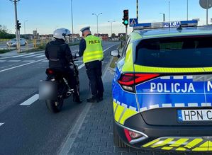 Policjant kontroluje motocyklistę, obok stoi radiowóz