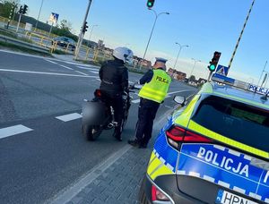 Policjant kontroluje motocyklistę, obok stoi radiowóz