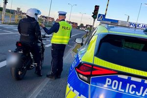 Policjant kontroluje motocyklistę, obok stoi radiowóz, wykonuje badanie trzeźwości