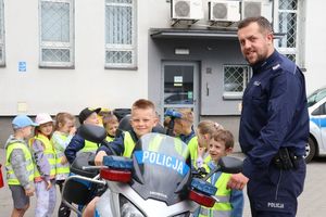 Policjanci z dziećmi pozuje przy motocyklu, jedno z dzieci siedzi na jednośladzie.