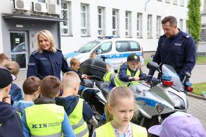 Trwa spotkanie, policjanci rozmawiają z dziećmi na placu komendy przy motocyklu.
