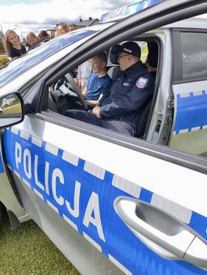 Policjant siedzi w radiowozie z dziećmi i opowiada im o wyposażeniu pojazdu