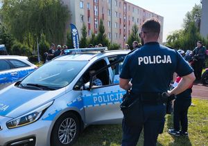 Policjant stoi obok otwartego radiowozu a w środku za kierownicą siedzi dziecko