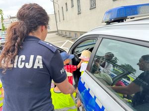 Policjantka stoi przy radiowozie, a dzieci wchodzą do środka.