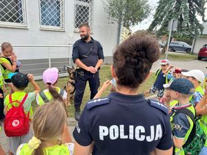 Policjanci rozmawiają z dziećmi, w tym przewodnik z psem do wykrywania narkotyków biorą udział w spotkaniu