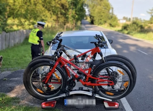 Policjantka rozmawia z kierowcą samochodu w białym kolorze, na tym samochodzie na jego tyle znajdują się przypięte do niego czerwone rowery.