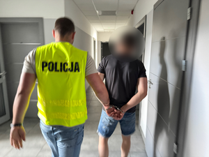 policjant prowadzi zatrzymanego korytarzem komendy