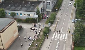 Zdjęcie wykonane dronem, na którym widoczne jest przejście dla pieszych i uczniowie idący do szkoły a także policjanci czuwający nad bezpieczeństwem pieszych.